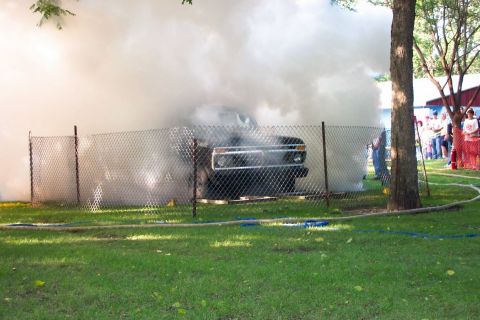 1977 Ford F-150 - A truck is heavily smoking behind a fence, with onlookers in the background.