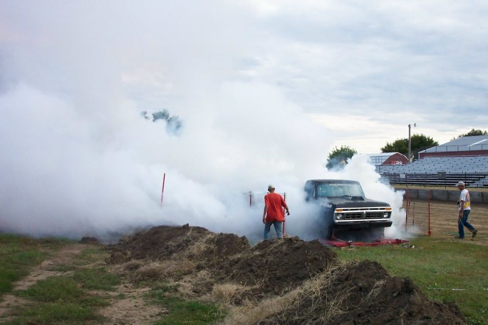 Primered 1970s Ford pickup doing a smoky burnout on a fairgrounds pad