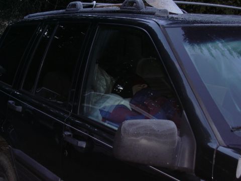 1991 Ford Bronco - Interior view of a dark-colored SUV with a person and blankets visible through the windows.