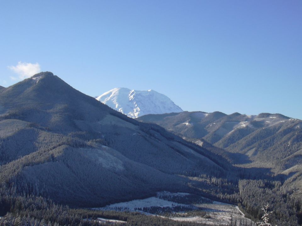 Snow-capped mountain peak behind dark, forested hills dusted with snow