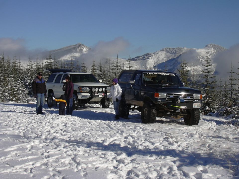 1991 Ford Bronco and a white SUV parked in snow with mountains behind