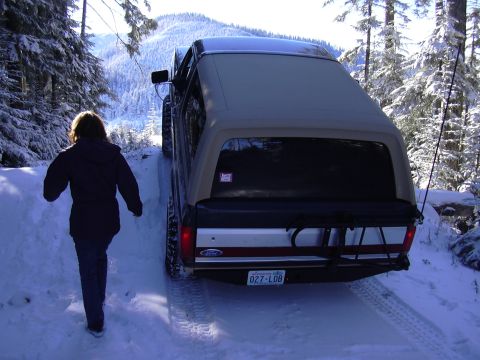 1991 Ford Bronco - A person walks away from a Ford Bronco with a camper shell on a snowy road surrounded by snow-covered trees.