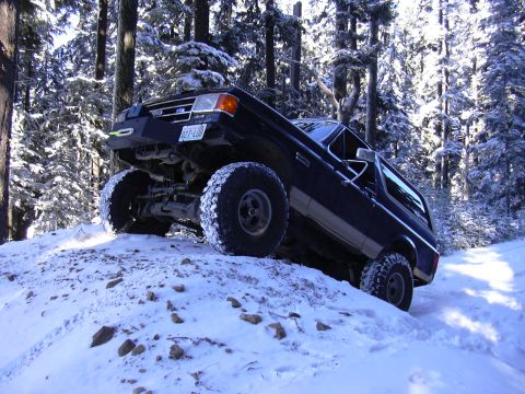 1991 Ford Bronco - A black Ford Bronco navigates a snow-covered incline amidst snow-laden trees.