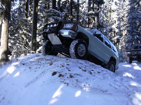 1991 Ford Bronco - Two SUVs navigate a snow-covered trail in a wooded area.