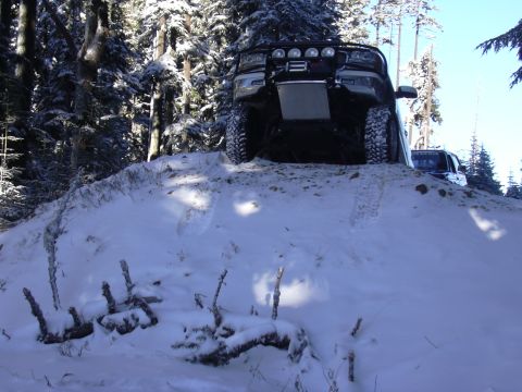 1991 Ford Bronco - A black SUV navigates a snow-covered hill in a forest, with another vehicle following behind.
