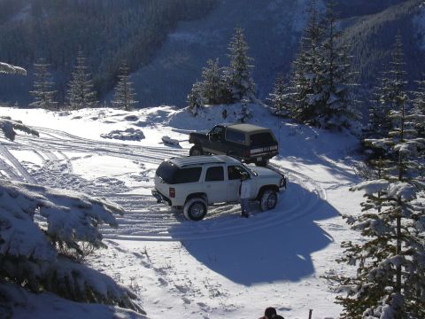 1991 Ford Bronco - Two SUVs navigate a snowy mountain trail, suggesting off-road adventure in a winter landscape.