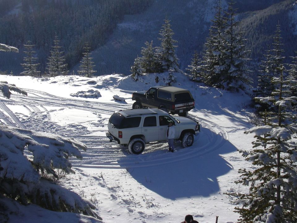 White SUV parked in snow with a person standing by the door; dark SUV behind it