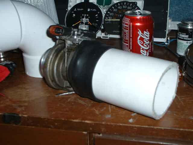 Automotive part, possibly a turbocharger, with white piping, next to gauges and a Coca-Cola can