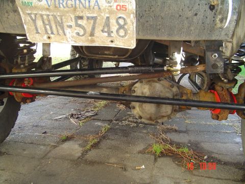 1989 Ford Bronco - The underside of a vehicle shows its heavy-duty suspension and steering components, including a differential and tie rods.