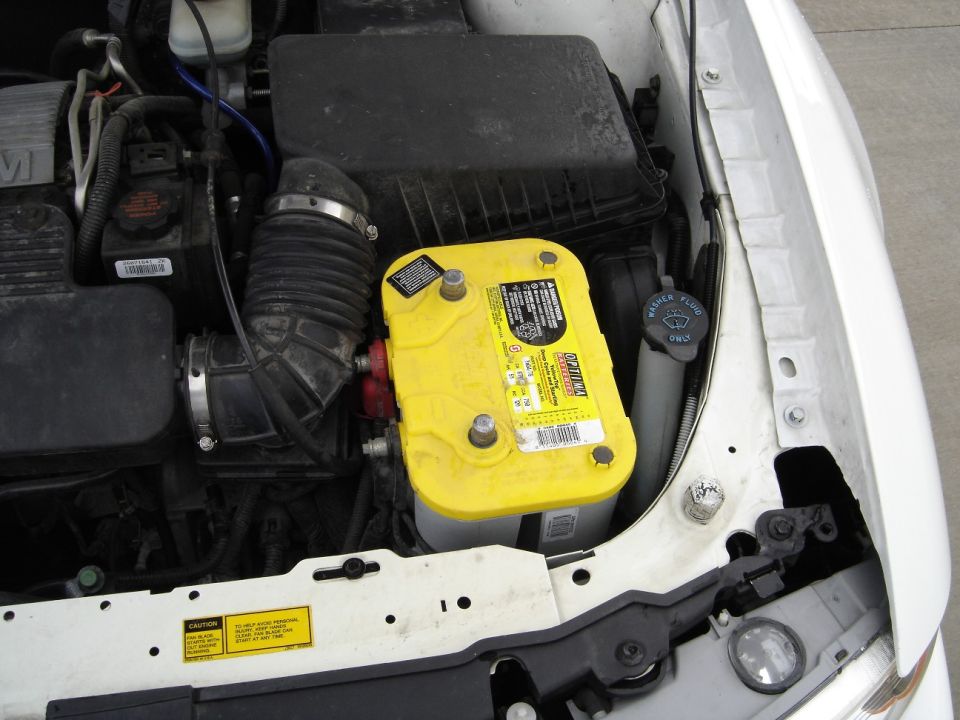 Yellow-top Optima battery installed in white car's engine bay beside airbox