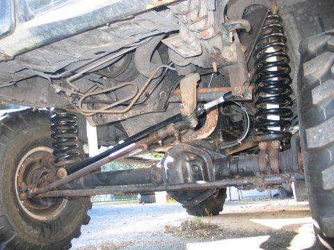 1992 Ford Bronco - Low-angle underside view of a lifted 4x4 front suspension showing black coil springs, a solid front axle with differential, tie rod and ste…