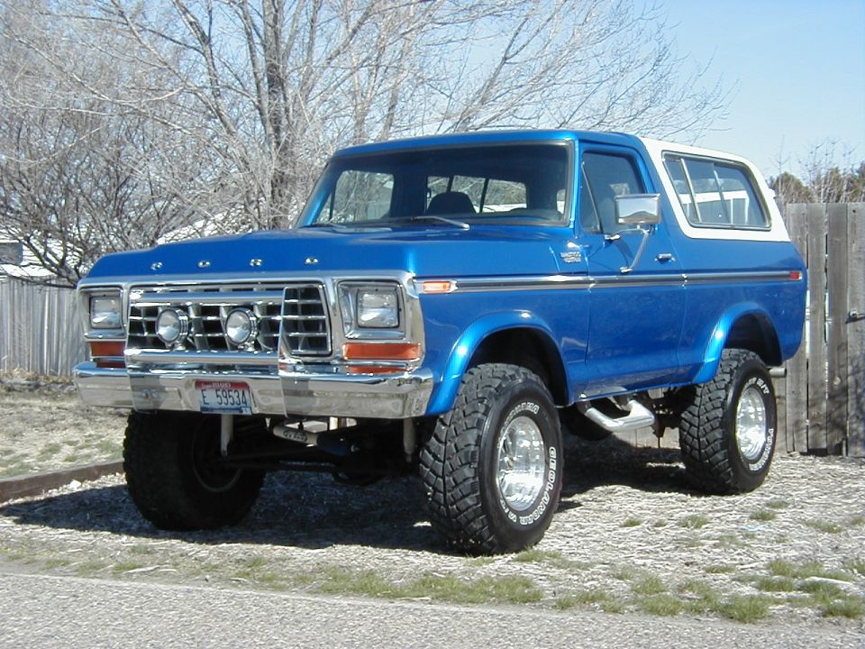 Blue 1978 Ford Bronco with a white hardtop, lifted suspension, and chrome wheels parked outdoors