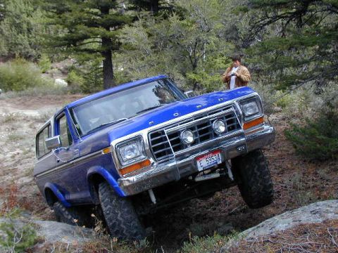 1978 Ford Bronco - A blue 1978 Ford Bronco navigates a challenging off-road course with a person standing in the background.