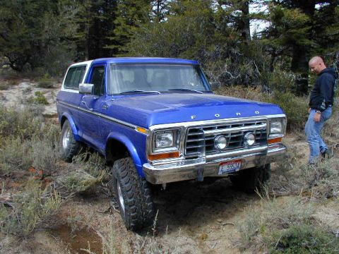 1978 Ford Bronco - 1978 Ford Bronco parked off-road with a man standing nearby. The vehicle is blue with a white top.
