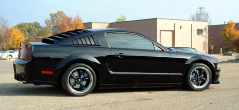 1973 Ford Ranchero - A black Ford Mustang is parked outside a building with autumn trees in the background.