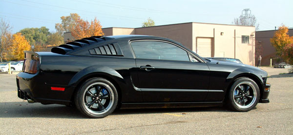 Black Ford Mustang with louvers on rear window and side windows, parked outside a building