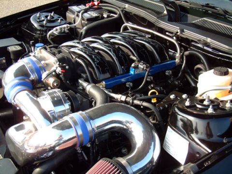 1973 Ford Ranchero - Close-up view of a modified engine bay a chrome intake system and a black intake manifold. Text is visible on a sticker.