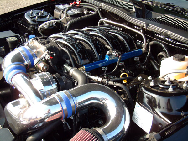 Engine bay with chrome intake, black manifold, and blue fuel rail. Text on a white sticker is visible