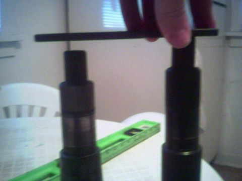 1987 Ford Bronco - Two black cylindrical parts are shown with a green ruler on a table.