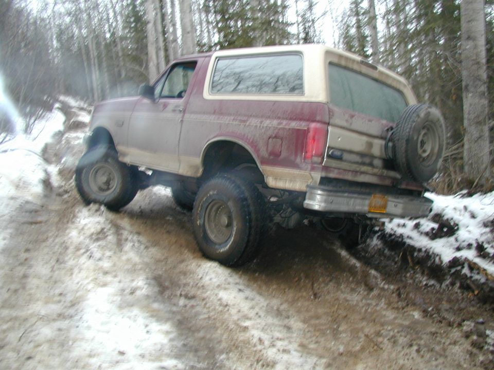 Maroon and tan lifted Ford Bronco flexing on a snowy muddy trail in the woods