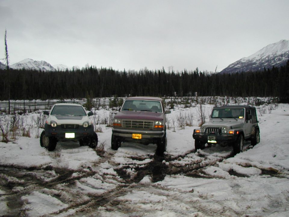 Lifted silver Isuzu Vehicross, maroon Ford pickup and silver Jeep Wrangler parked in snow