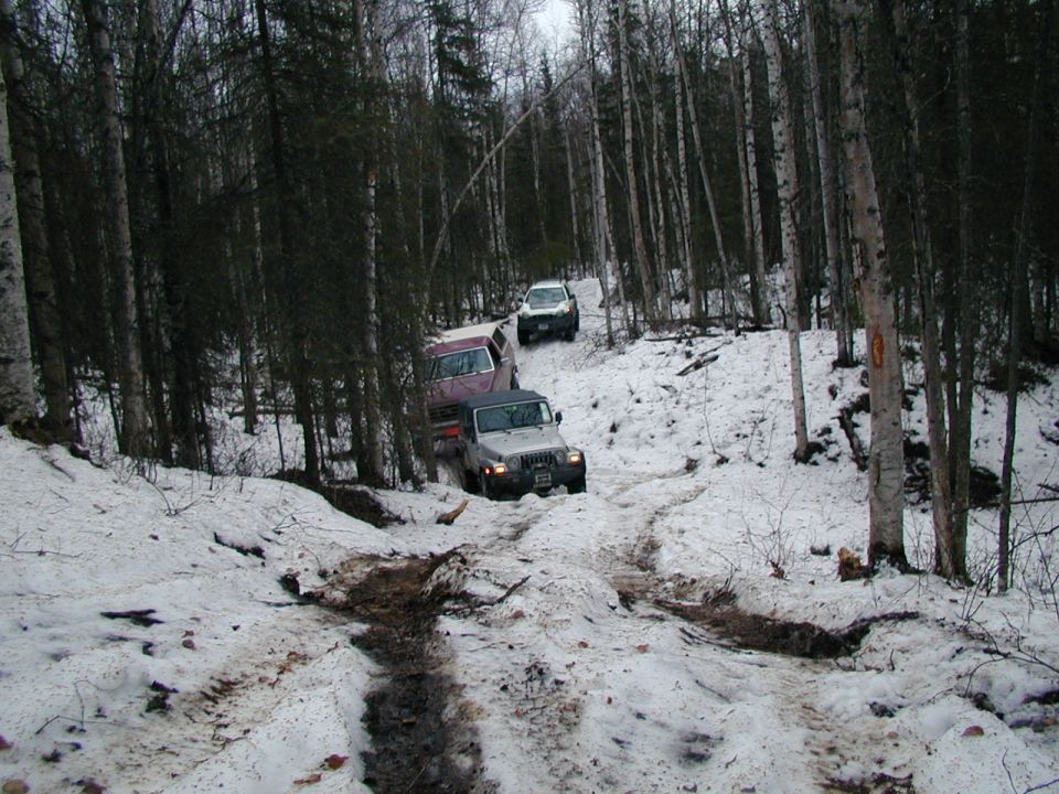 Three SUVs navigate a muddy and snowy path through a dense forest