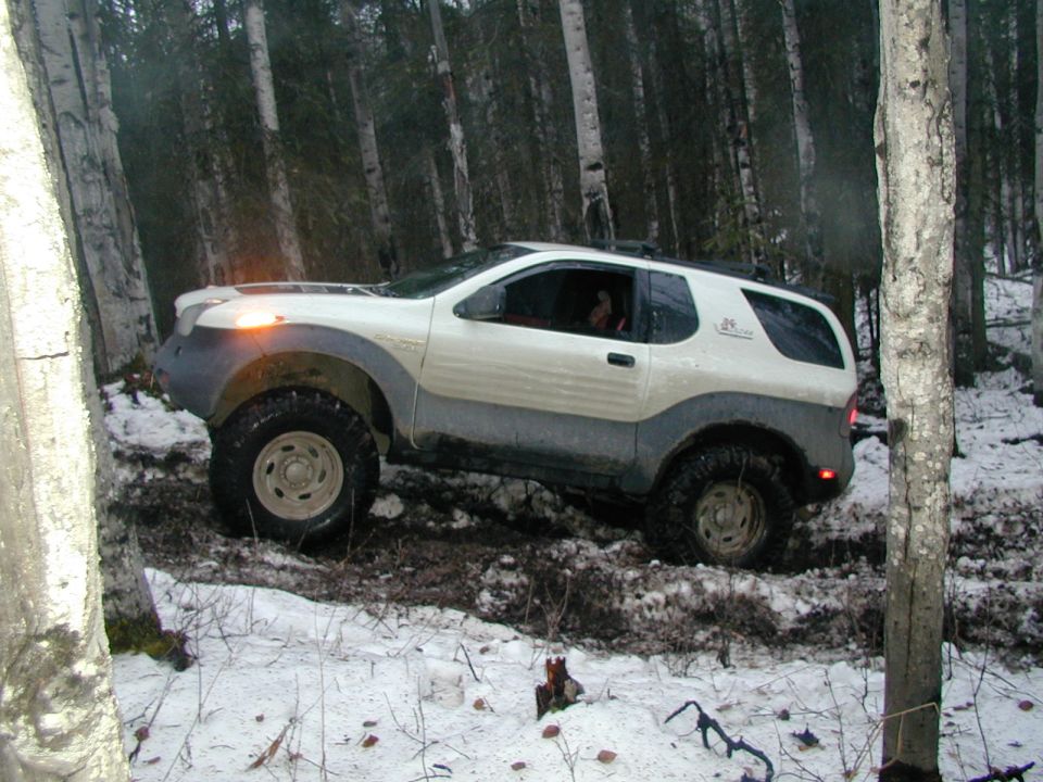 Lifted white Isuzu VehiCross on mud tires in a snowy birch forest, side view