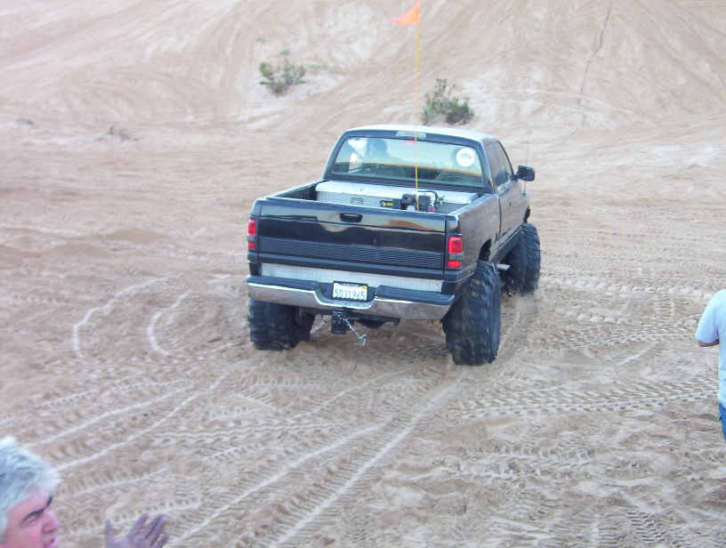 Lifted black pickup truck on oversized tires parked on sand dunes