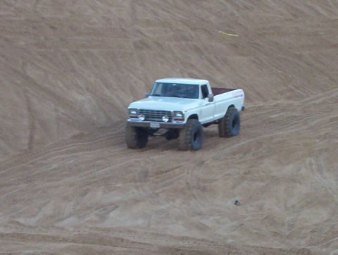 2000 Ford F-450 - A white pickup truck navigates sandy terrain, its large tires kicking up dust.