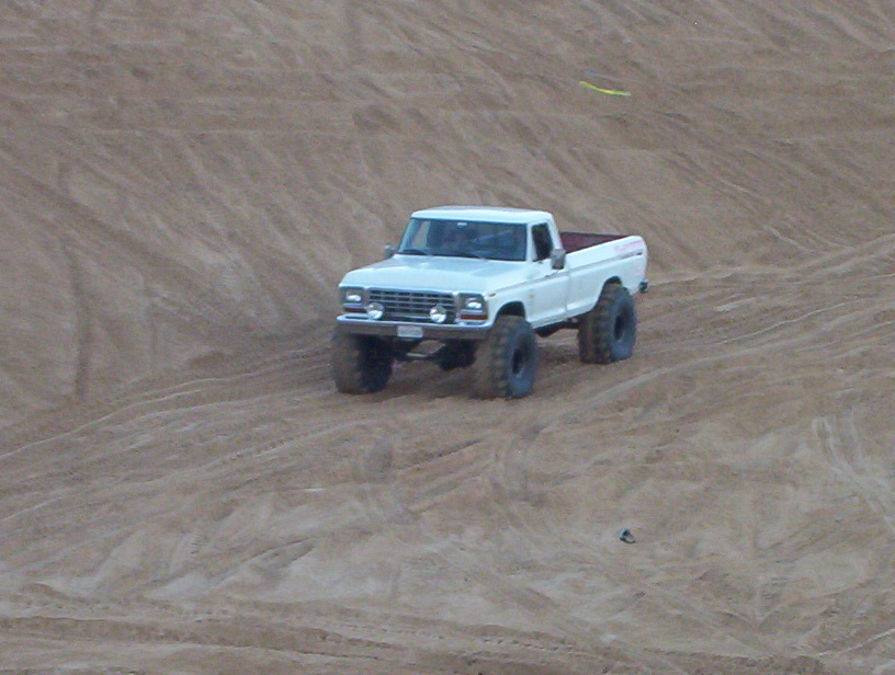 White pickup truck with large tires driving on sand dunes