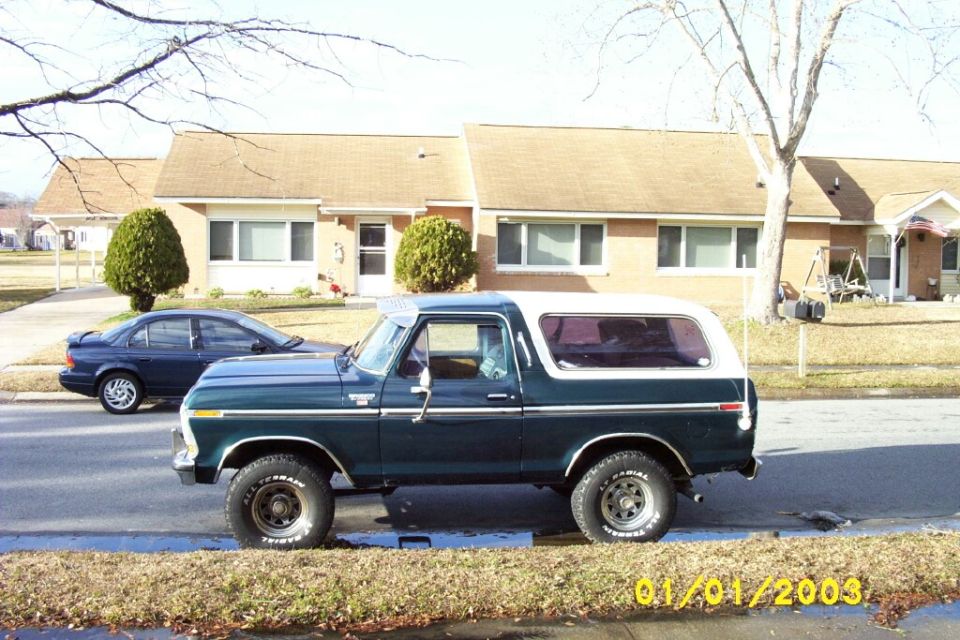 Side view of a dark green Ford Bronco with white roof and white-letter tires parked on a street