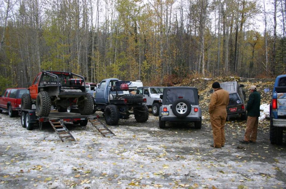 Silver 2003 Jeep TJ rear view, spare tire mounted on tailgate, aftermarket bumper, in a snowy lot with trees