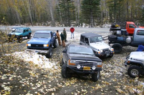2003 Jeep TJ - A group of off-road vehicles are gathered on a dirt road with trees in the background.