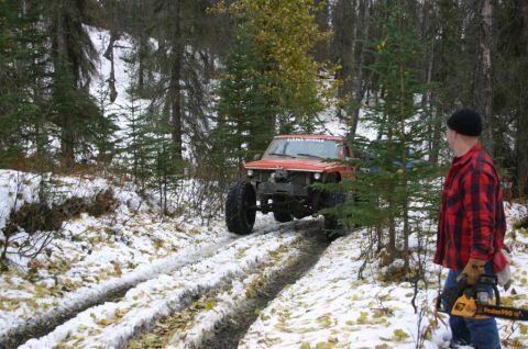 2003 Jeep TJ - A man watches an off-road vehicle navigate a snowy forest path, with fallen leaves scattered on the ground.
