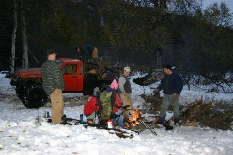 2003 Jeep TJ - People gathered around a campfire next to a red pickup truck in a snowy wooded area.