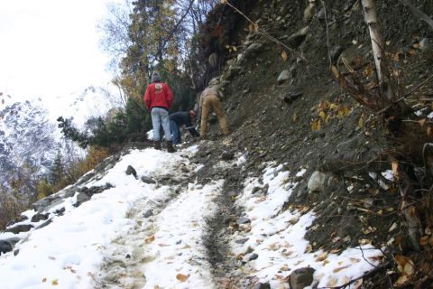 2003 Jeep TJ - Three individuals navigate a snow-dusted mountain path, surrounded by trees and rocky terrain.