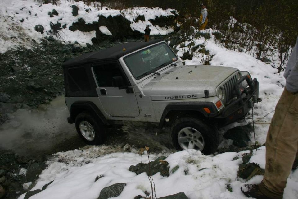 Silver Jeep Wrangler Rubicon driving through muddy water with snow on the ground