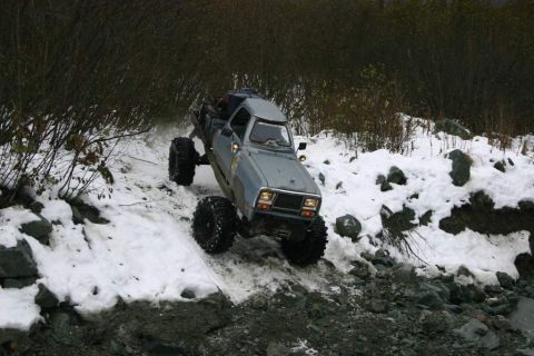 2003 Jeep TJ - Modified pickup truck with oversized tires tackles a challenging off-road course in snowy conditions.