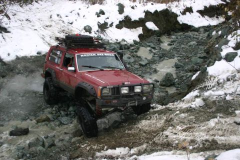 2003 Jeep TJ - A red Jeep Cherokee XJ navigates a challenging off-road trail in a snowy, rocky environment.