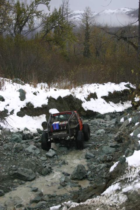 2003 Jeep TJ - An off-road vehicle navigates a challenging, rocky path in a snowy, wooded environment.