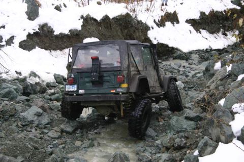 2003 Jeep TJ - A green 2003 Jeep TJ navigates a rocky, snow-dusted trail, demonstrating its off-road capabilities.