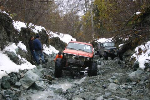 2003 Jeep TJ - Two off-road vehicles navigate a challenging, rocky path with snow on the sides.