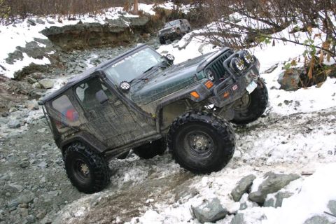 2003 Jeep TJ - Two Jeeps tackle a challenging off-road course with snow and rocks on the path.