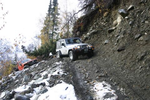 2003 Jeep TJ - Two Jeeps navigate a challenging off-road trail with snow and loose rocks.