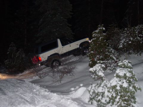 1986 Ford Bronco - A white SUV navigates a snowy incline in a wooded area after dark.