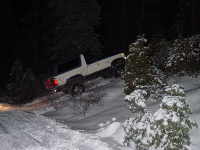 White SUV driving up a snowy hill at night, surrounded by trees