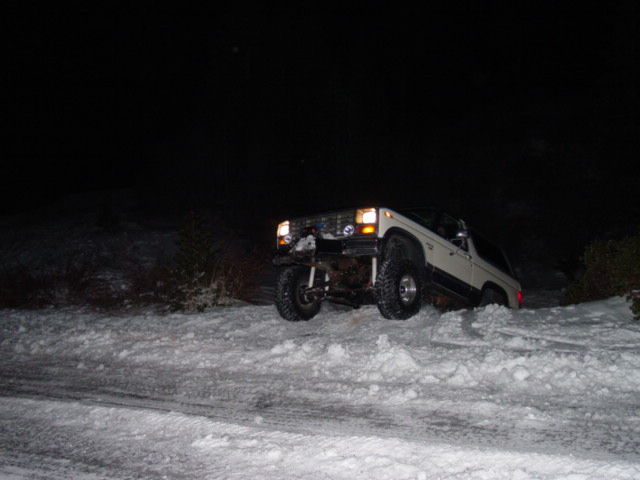 White SUV with aftermarket bumper and large tires on a snowy incline at night