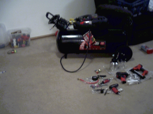 Black air compressor with various pneumatic tools and accessories on carpeted floor