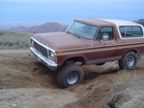 1978 Ford Bronco - A brown 1978 Ford Bronco navigates a dirt track in a hilly, arid landscape.