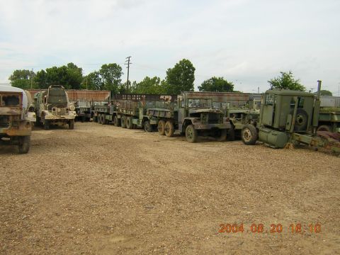 1984 Chevrolet Blazer - Multiple olive drab military trucks are parked in a lot under an overcast sky.